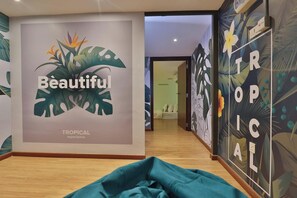 A hallway with a tropical-themed wall mural, a bed, and a wooden floor. - Trevor Hotel by I Housing (Malacca City)
