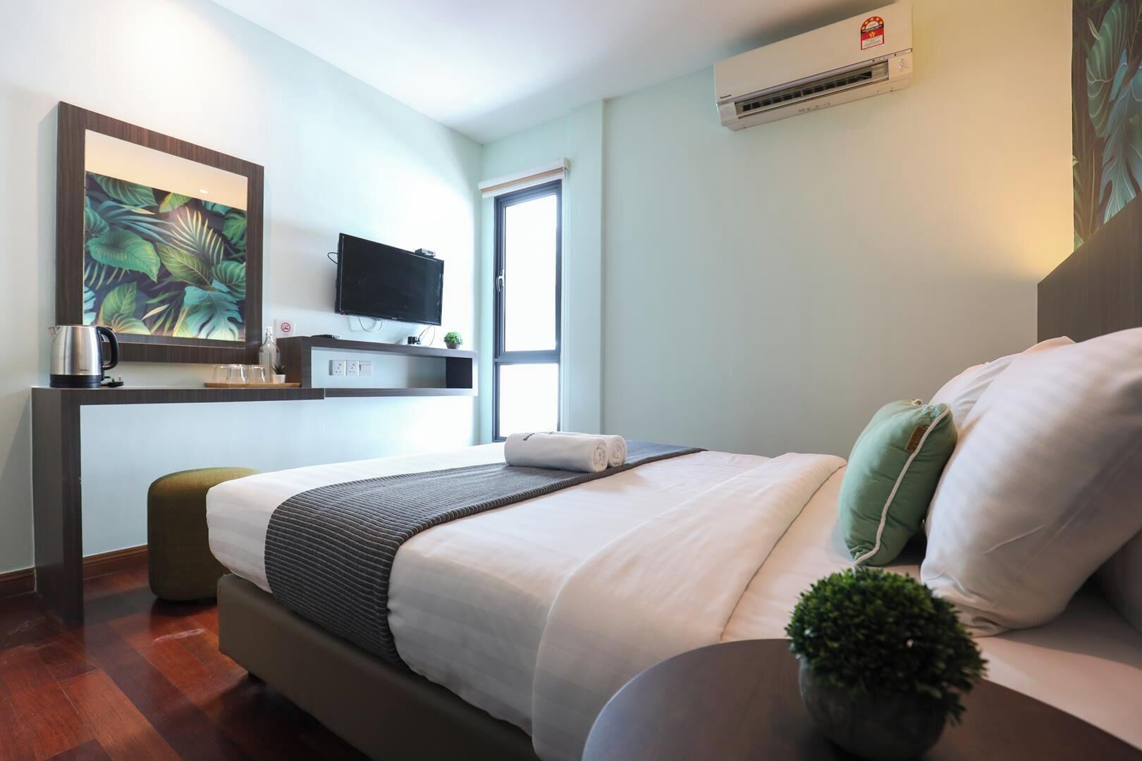 A hotel room with a bed, a TV, a coffee maker, a small table, and a potted plant.