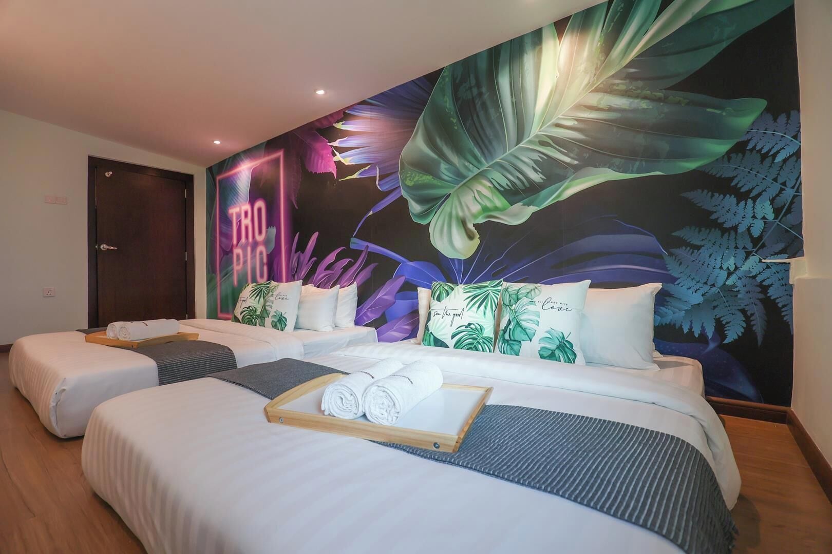 A hotel room with two beds, a large tropical-themed mural, and a wooden door.