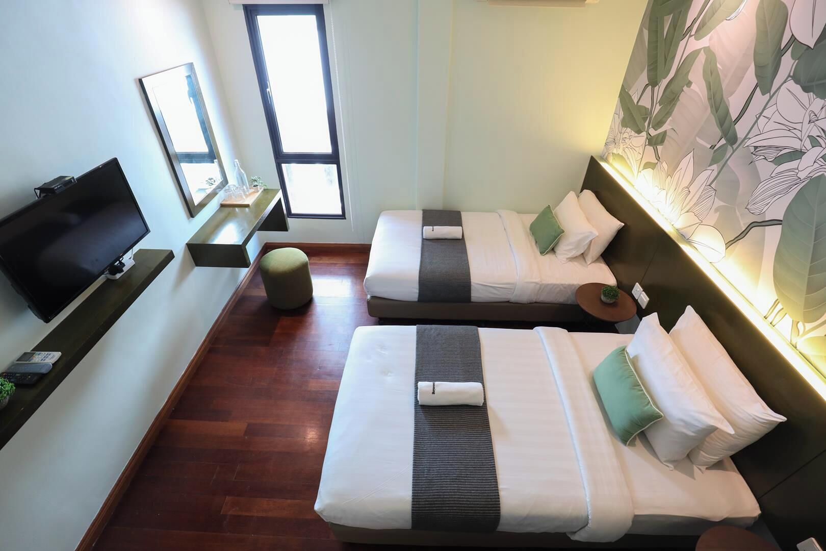 A hotel room with two beds, a TV, a small table, and a window.