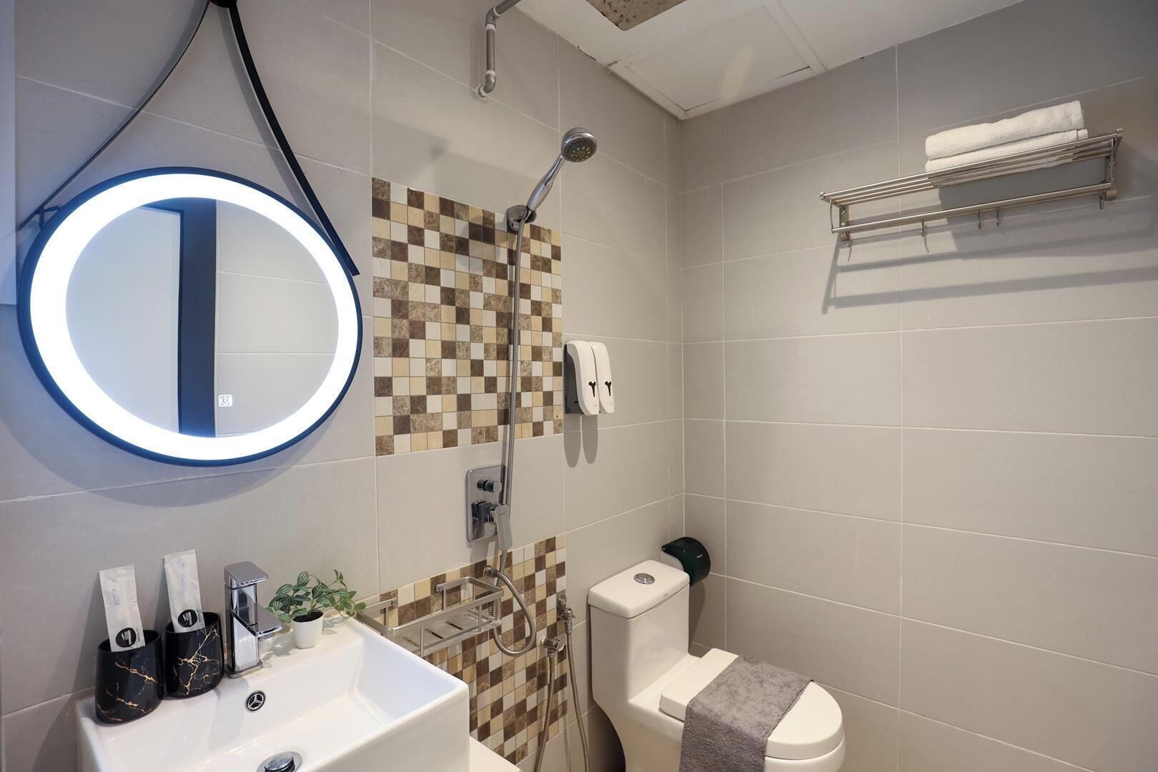 Un baño moderno con un espejo redondo, ducha, inodoro y toallero.