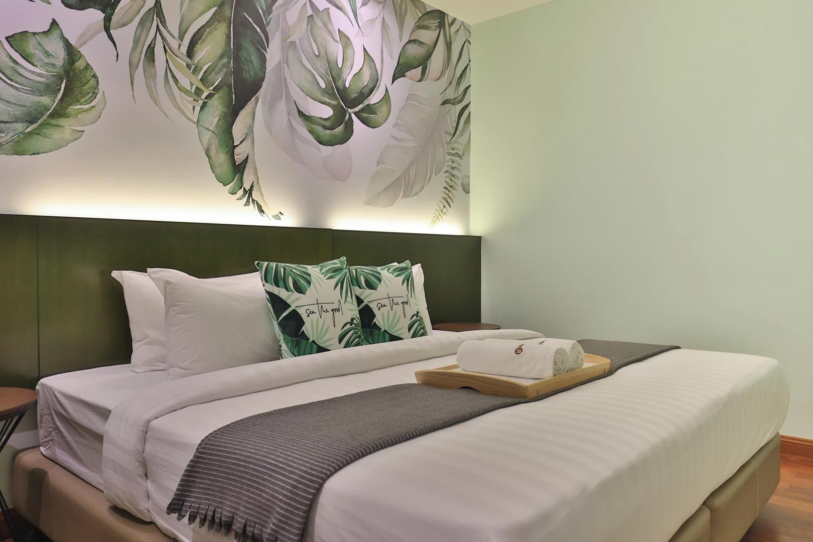A neatly made bed with a pillow, a bedside table, and a wall with a leaf pattern.