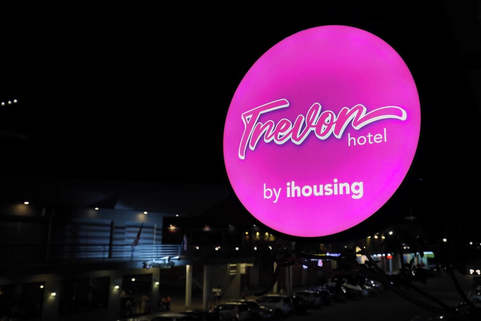 A neon sign for the 'Trevon hotel by ihousing' with a modern building in the background.