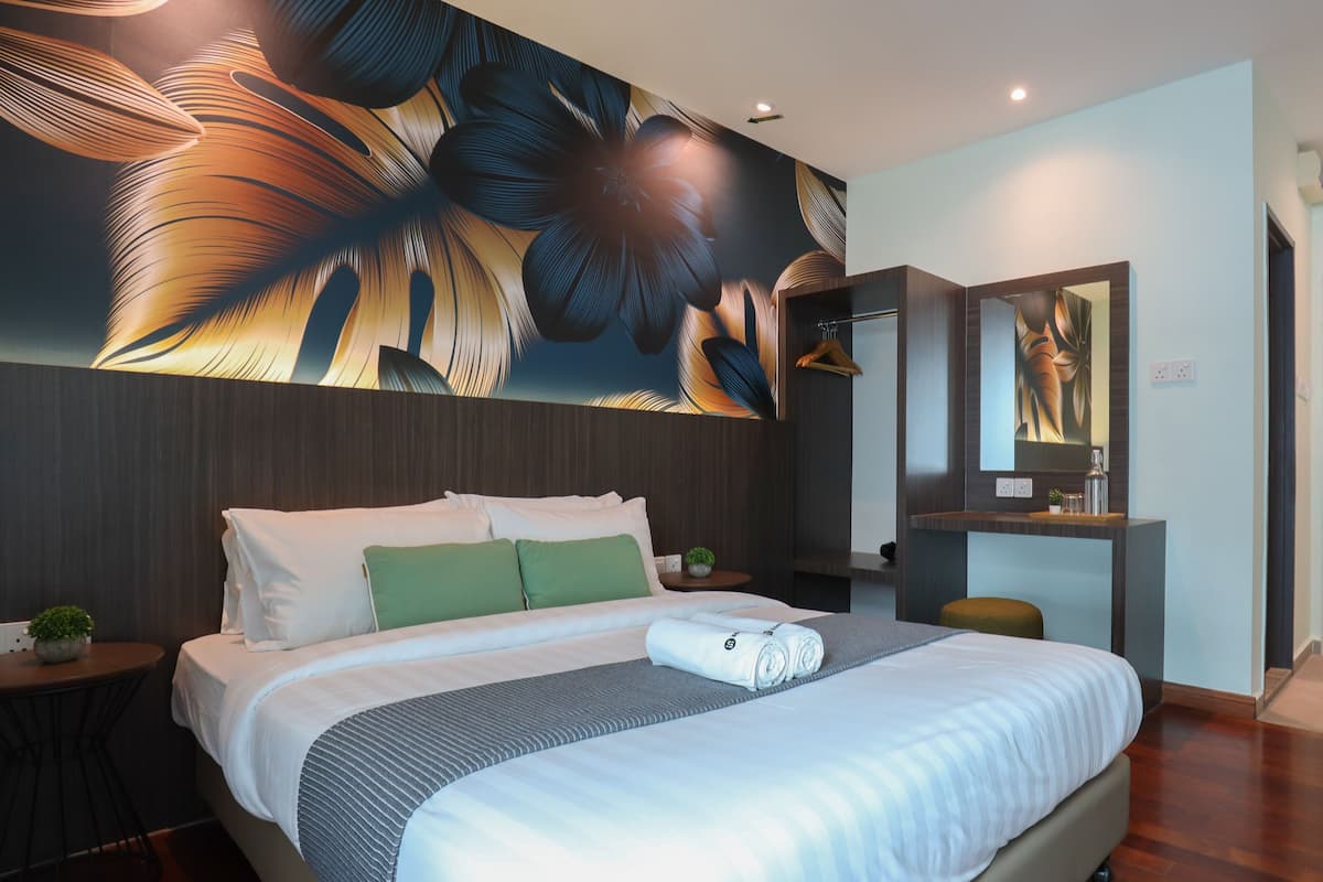 A modern hotel room with a large bed, a small side table, a mirror, and a wall with a large floral mural.