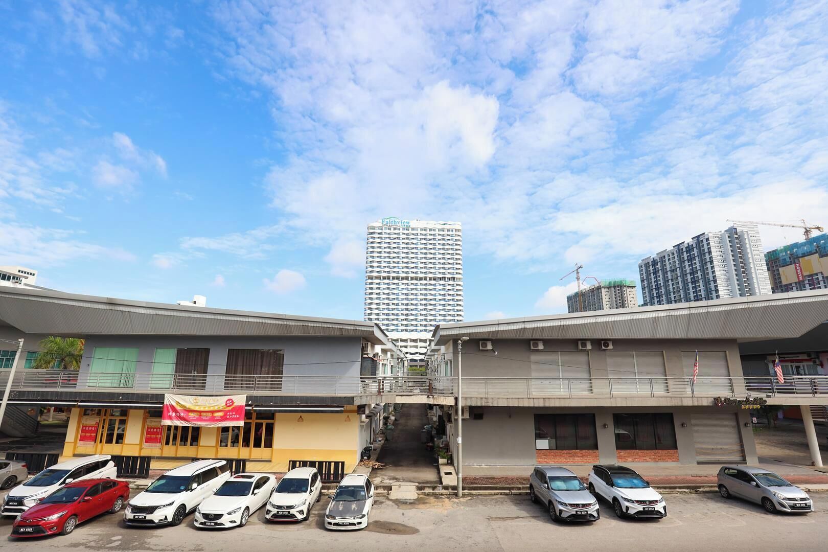 A street view with a row of parked cars, a building with a sign, and a tall skyscraper in the background.