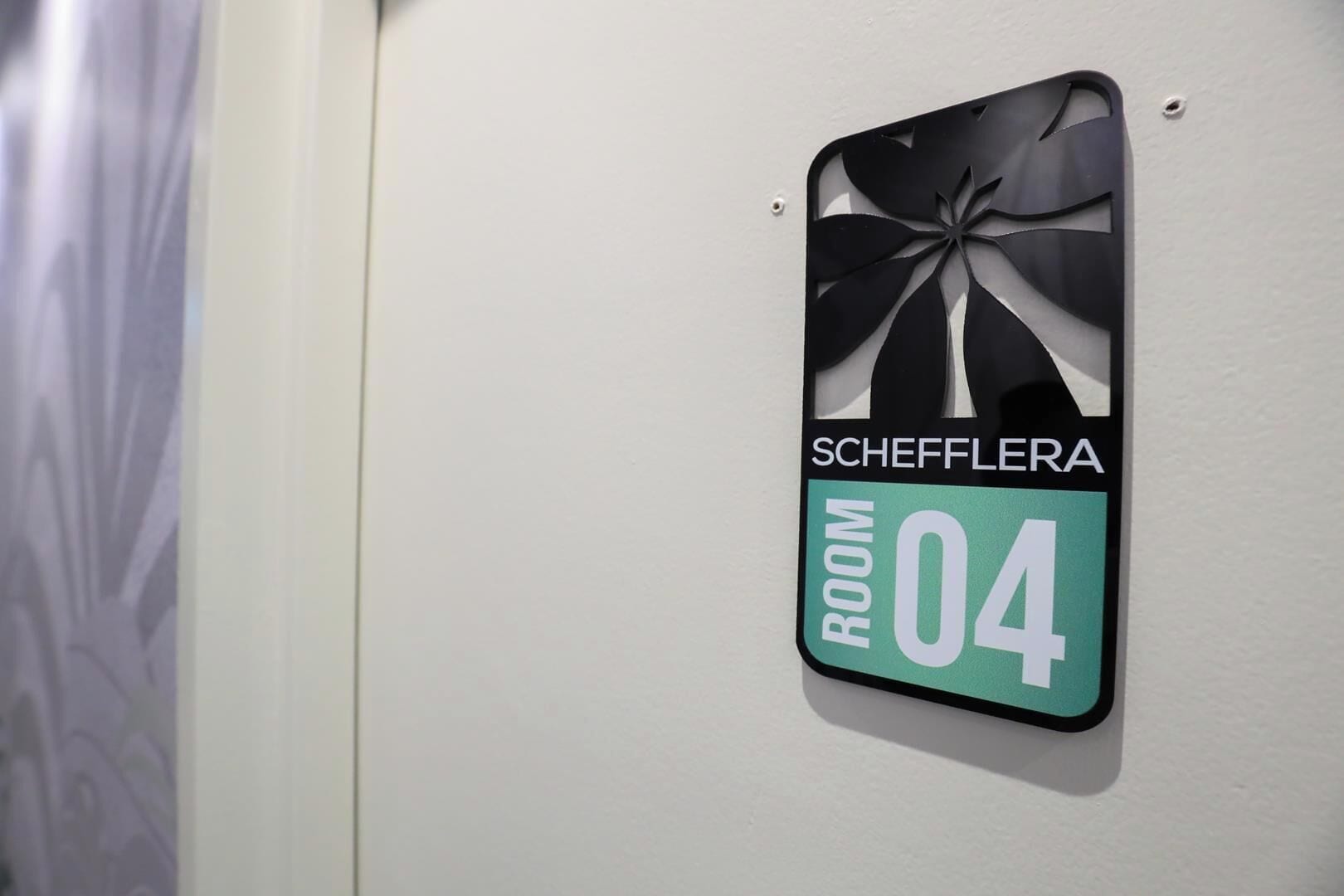 A hotel room sign with 'Schefflera' and 'Room 04' indicating the room's name and number.