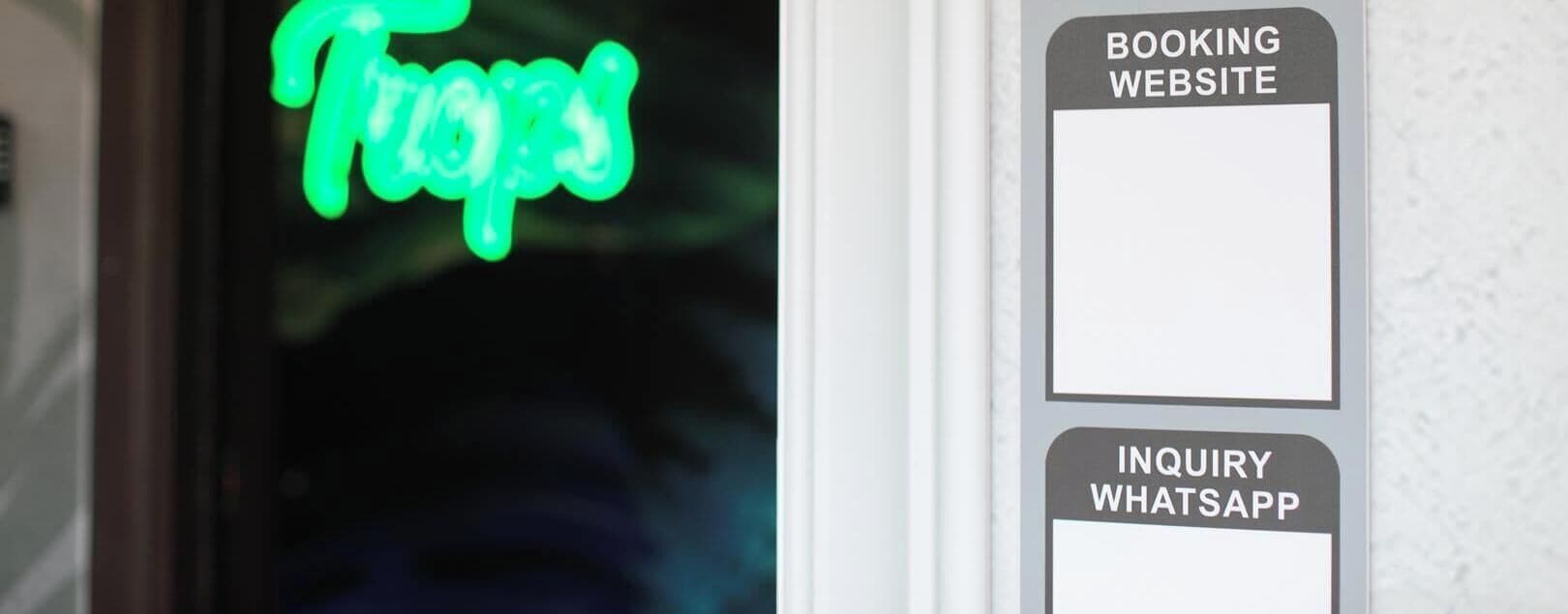 A neon sign with the word 'Tropes' and two blank labels for 'BOOKING WEBSITE' and 'INQUIRY WHATSAPP'.