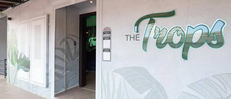 A hotel entrance with a sign reading 'The Tropics' and a glass door leading inside.