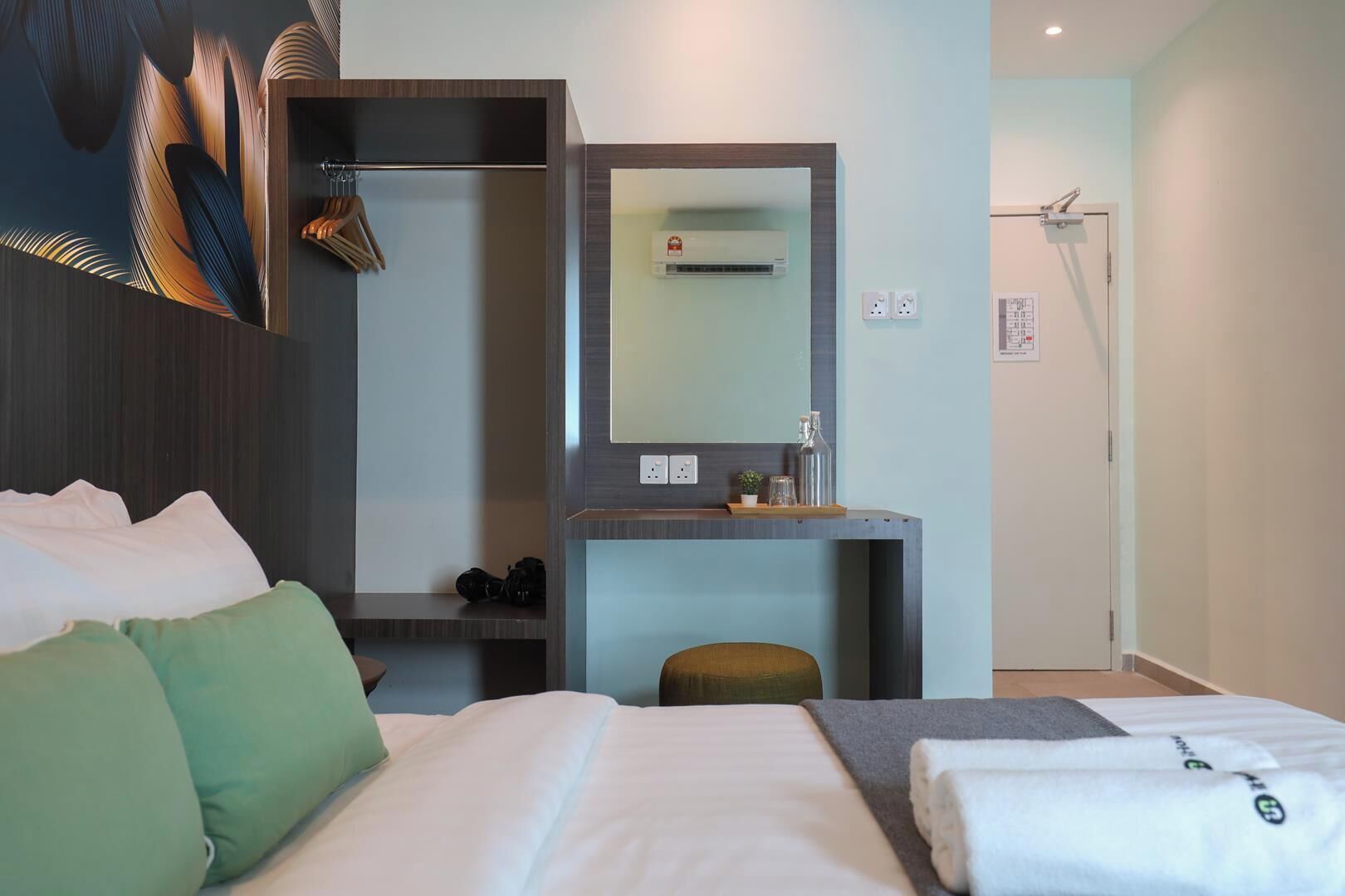A hotel room with a bed, a desk with a mirror, a small stool, and a shower area.