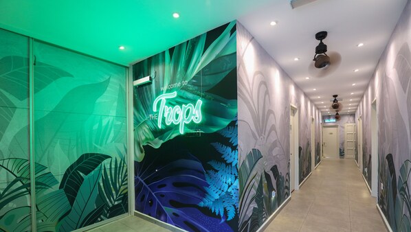 A hallway with a green-themed mural, a neon sign reading "Welcome to The Trips," and a ceiling fan. - Trevor Hotel by I Housing (Malacca City)