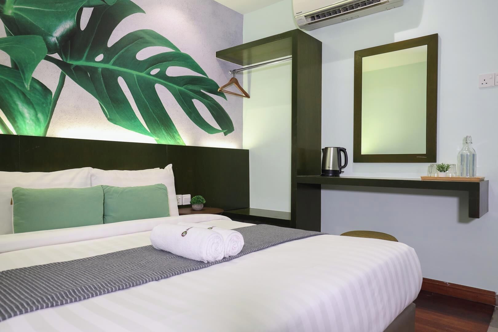 Una camera d'albergo con un letto, uno specchio grande, una macchina per il caffè e una pianta.