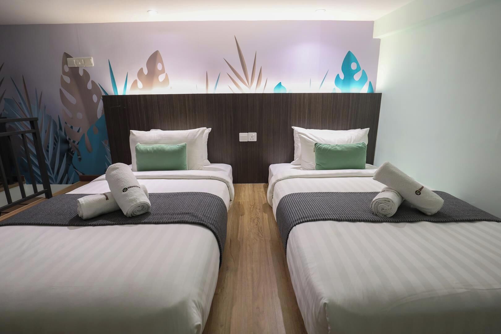 A hotel room with two beds, each with a pillow and a rolled towel.