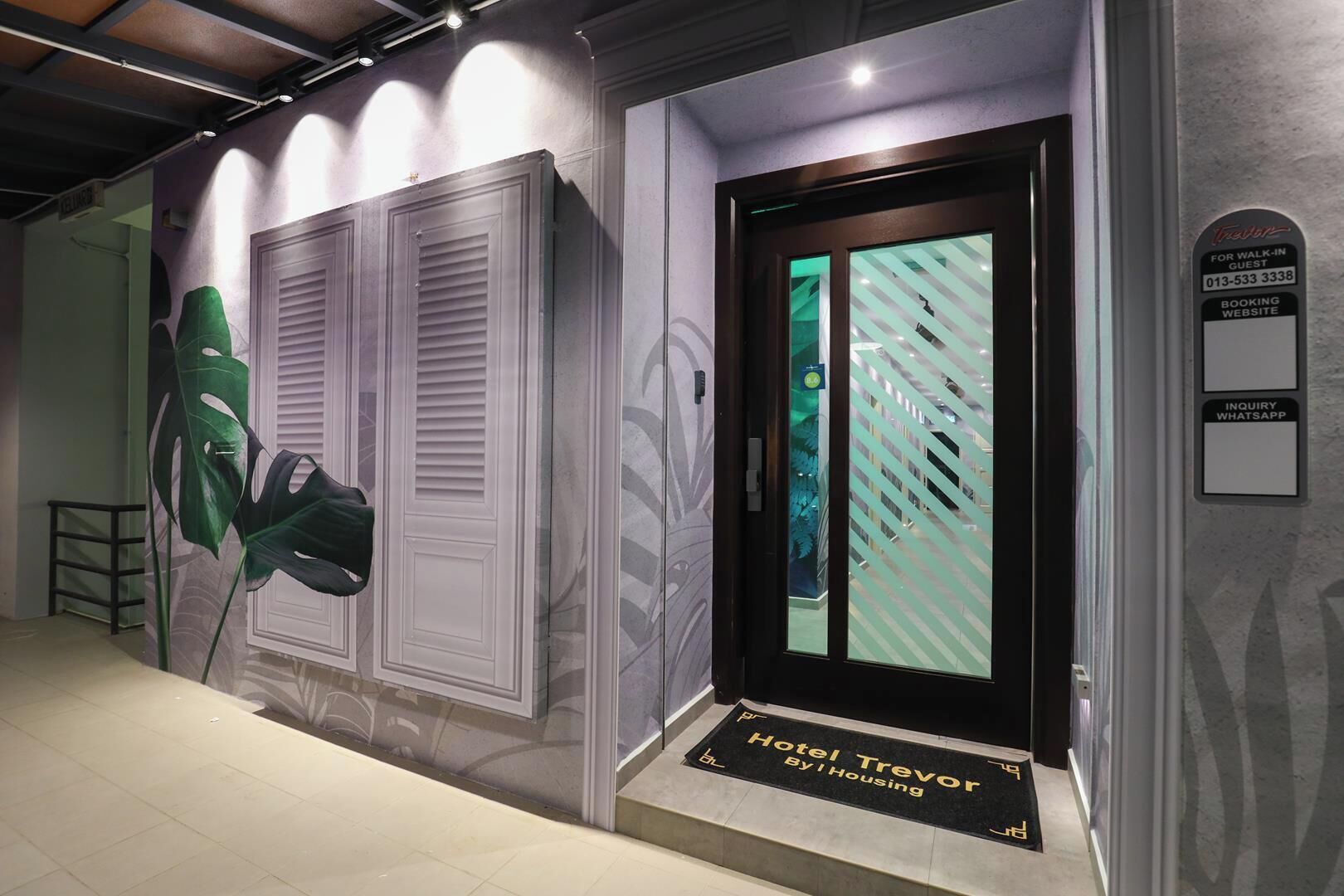 A hotel entrance with a modern design, including a large green plant, a door with a striped pattern, and a sign indicating a walk-in guest service area.