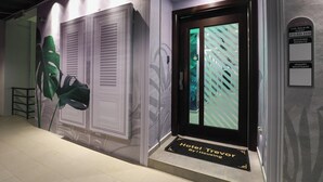 A hotel entrance with a modern design, including a large green plant, a door with a striped pattern, and a sign indicating a walk-in guest service area. - Trevor Hotel by I Housing (Malacca City)