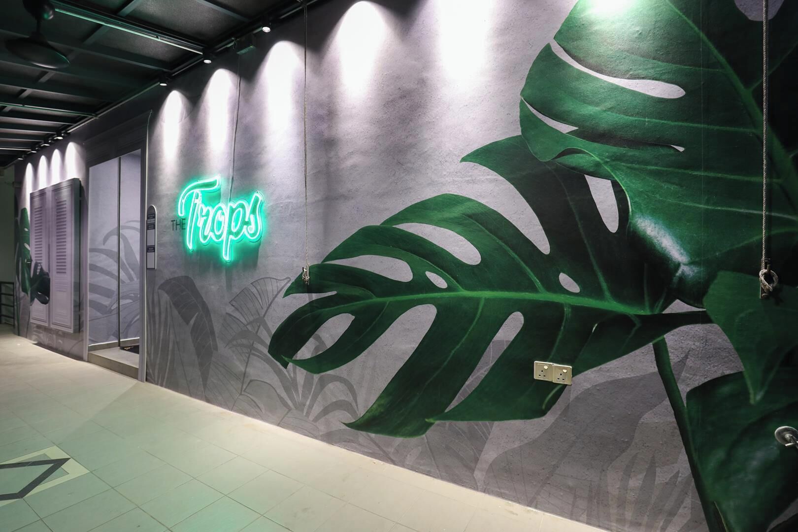 A wall with a neon sign reading 'The Tops' and a large green plant.