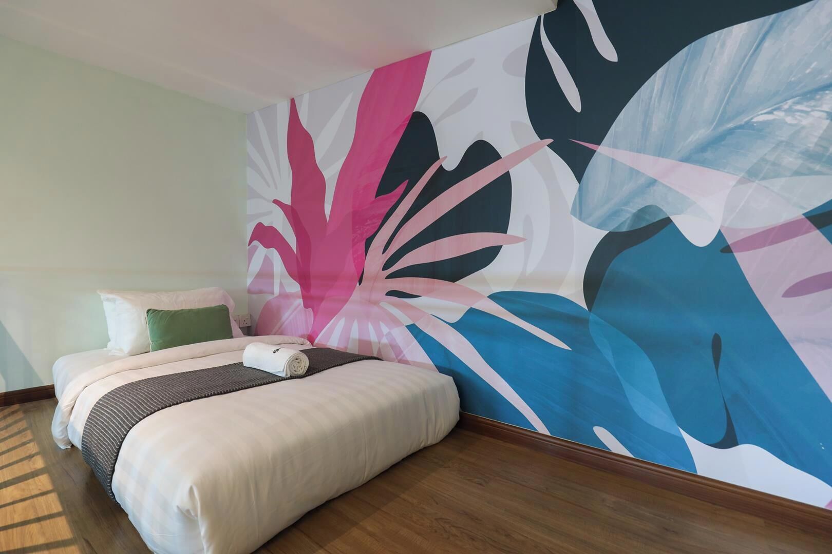 A hotel room with a bed, a large abstract wall mural, and a wooden floor.