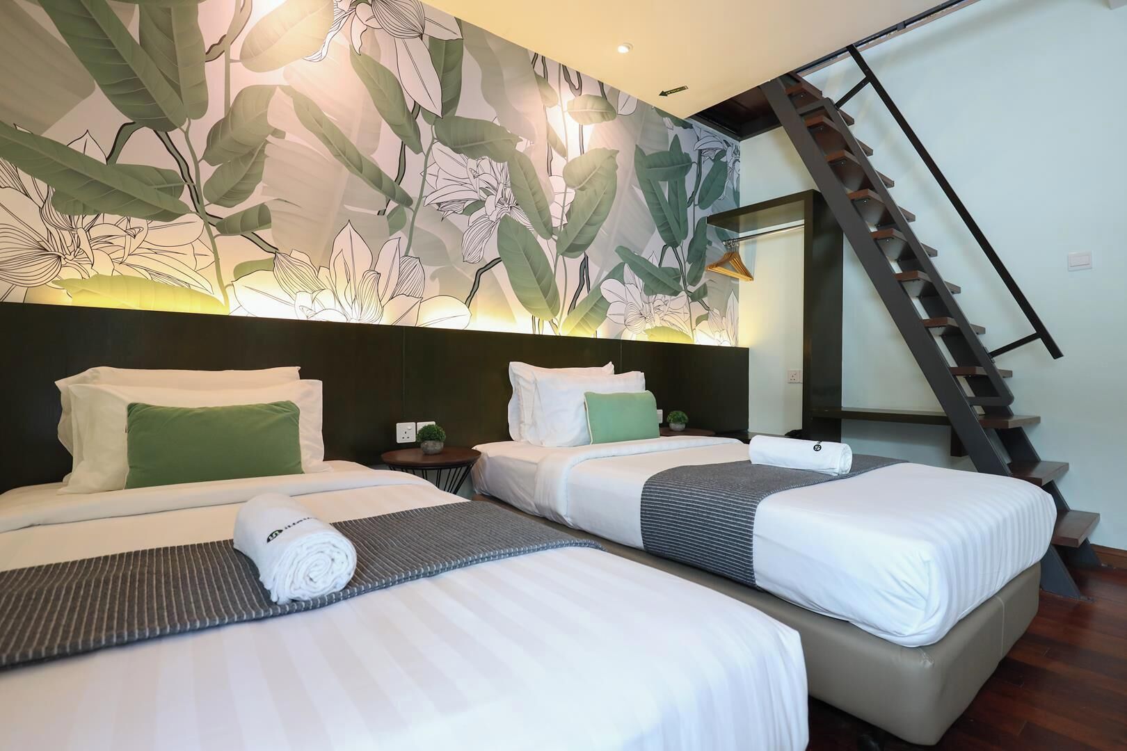 A hotel room with two beds, a nightstand, a small table with a plant, and a staircase.