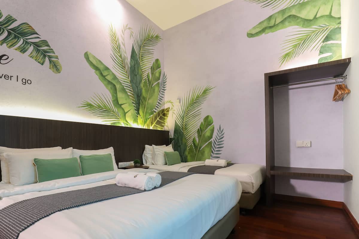 A hotel room with two beds, a headboard, and a wall mural with tropical leaves.