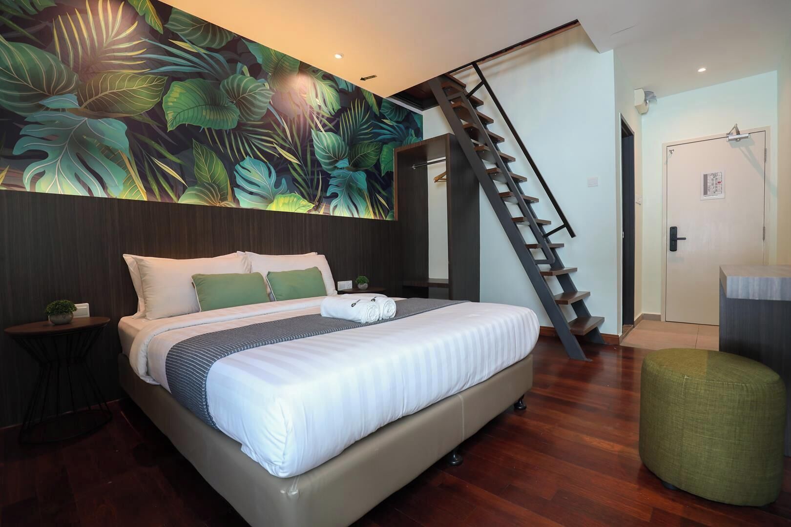 A modern bedroom with a large bed, a staircase, and a tropical leaf mural on the wall.