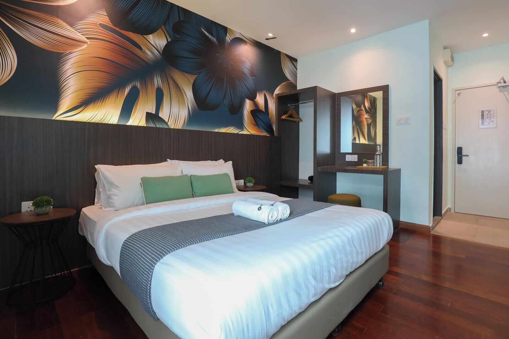 A modern hotel room with a large bed, a bedside table with a plant, a mirror, and a wall with a floral mural.