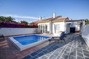Une piscine dotée d’une terrasse carrelée, d’un espace salon extérieur et d’un bâtiment blanc avec un toit recouvert de tuiles.