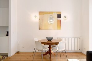 Un coin repas avec une table ronde en bois, des chaises blanches et un luminaire suspendu.