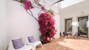 A patio with two white chairs, a table, and a large flowering plant. - Villa 'Casa Rosa' with Private Terrace and Wi-Fi (São Brás de Alportel)