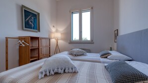 Un dormitori amb dos llits, un armari de fusta, una barra penjant, una finestra i un quadre a la paret.