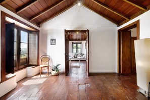 Una habitación con suelo de madera, un sofá blanco, una silla y una ventana con persianas.