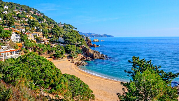 Un pueblo costero con playa, casas en una ladera y costa rocosa.
