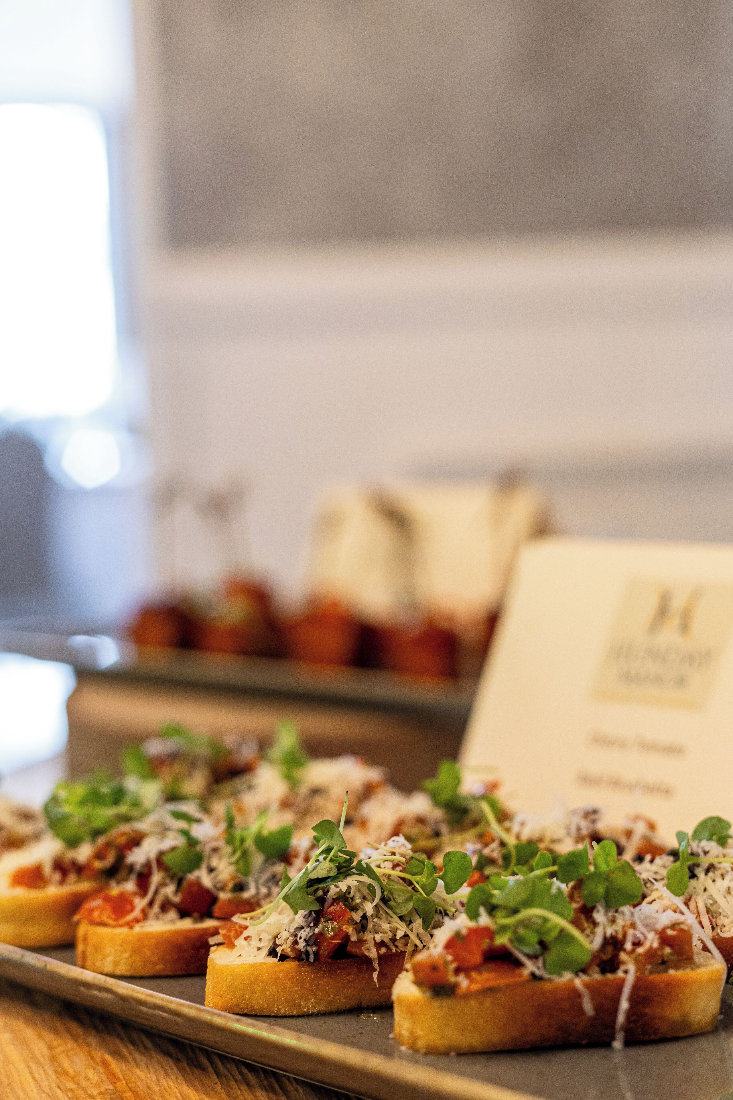A tray of bruschetta with various toppings, including cheese and greens, on a wooden table.