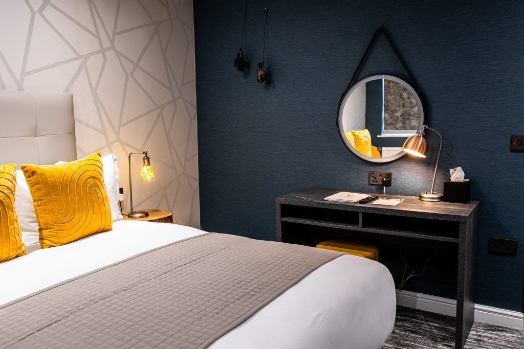 Una camera d'albergo con un letto, una lampada da comodino, una scrivania, uno specchio e decorazioni a parete.