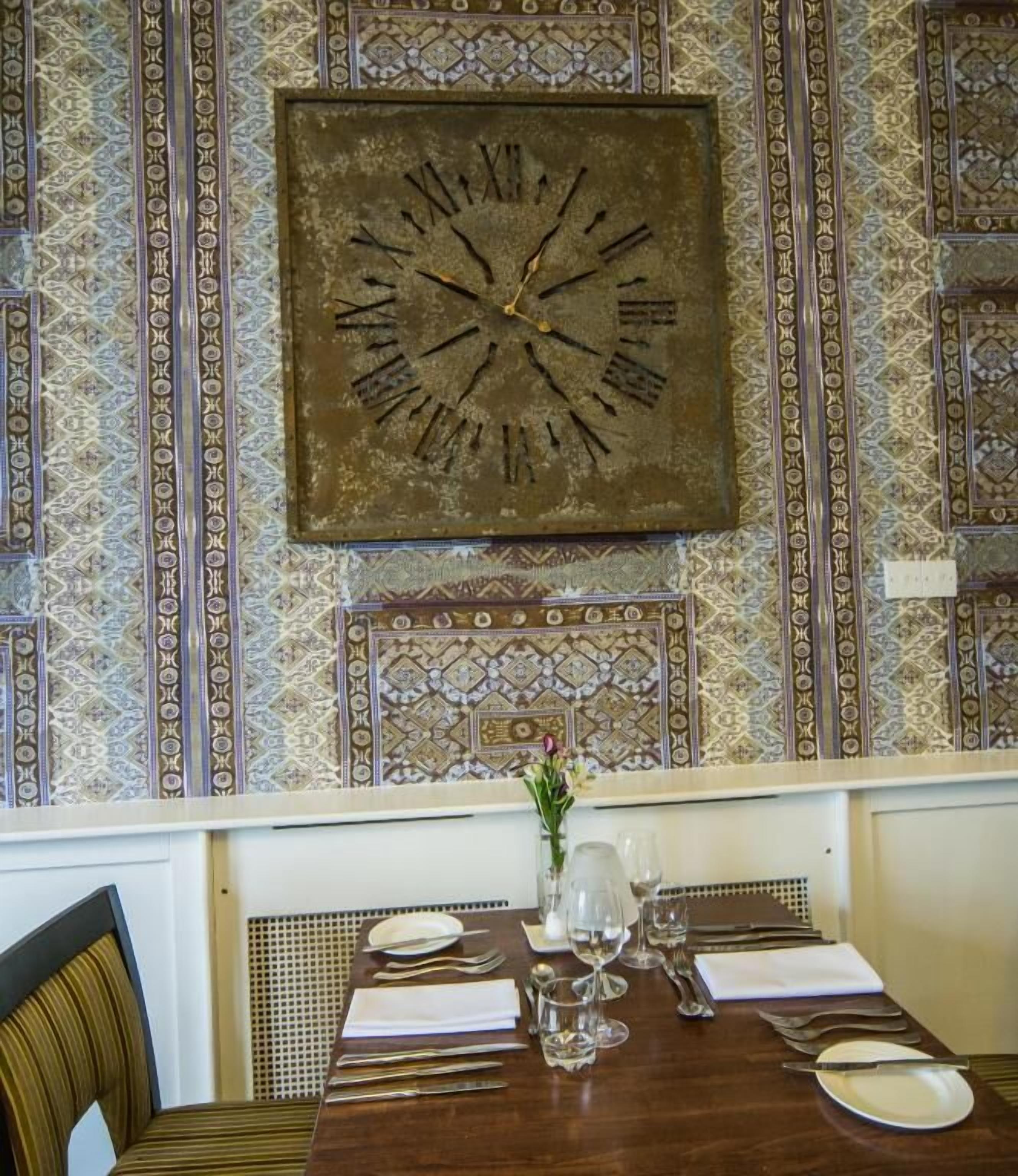 A dining table set with plates, cutlery, and glasses, with a large clock above it.