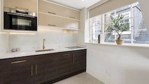 Une cuisine moderne avec des meubles de couleur bois foncé, un four encastré et une fenêtre donnant sur des immeubles.