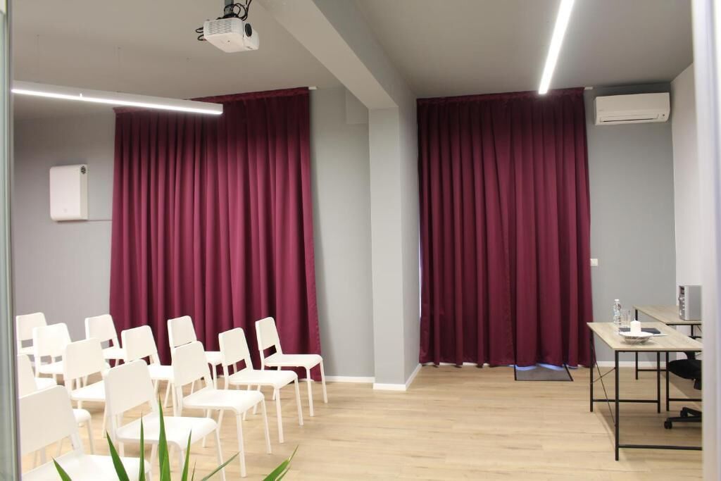 A conference room with white chairs, a projector, and a table with a laptop and water bottle.