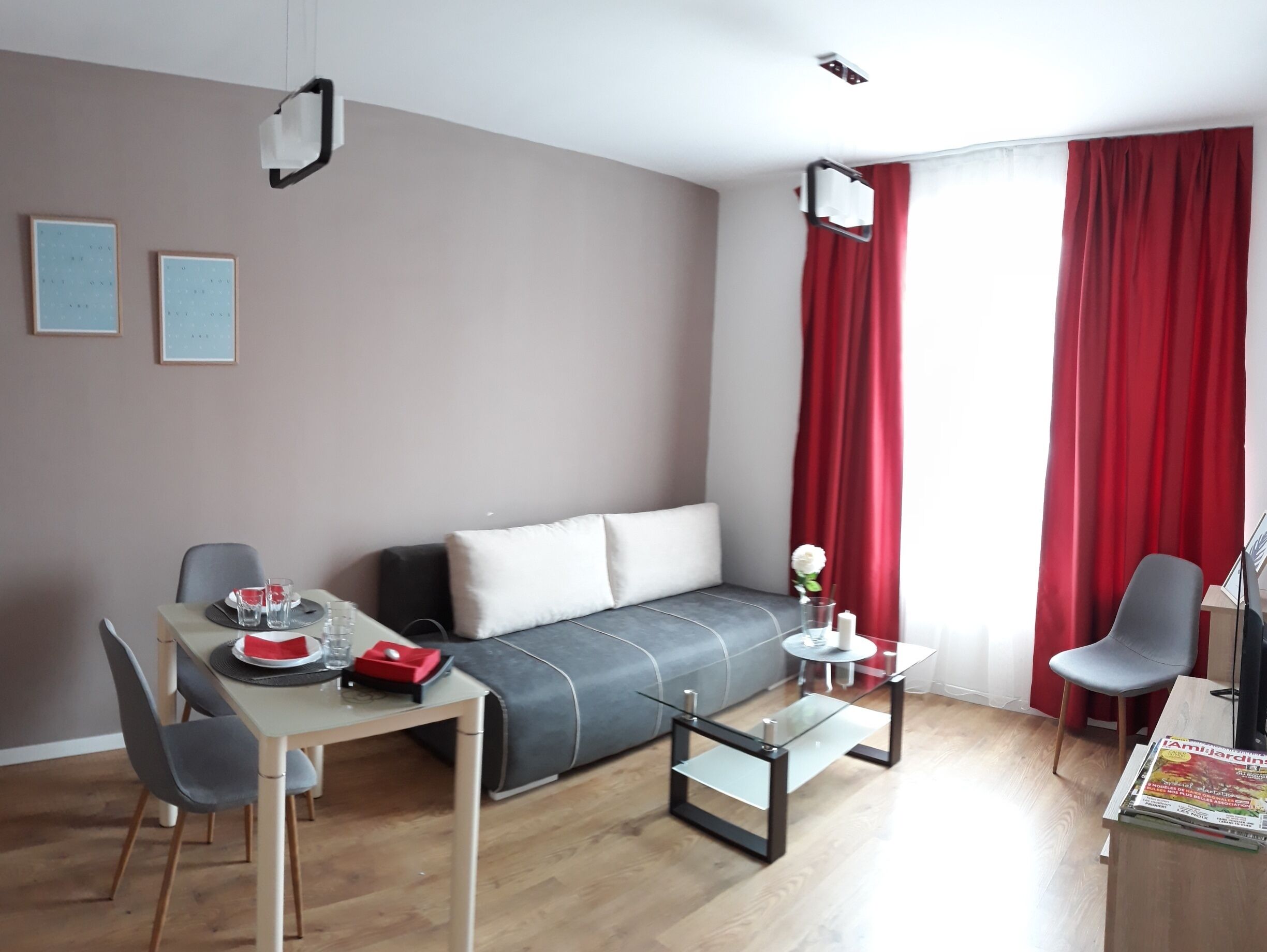 Una habitación moderna con sofá, una mesa de comedor con sillas, una mesita auxiliar y una ventana con cortinas rojas.