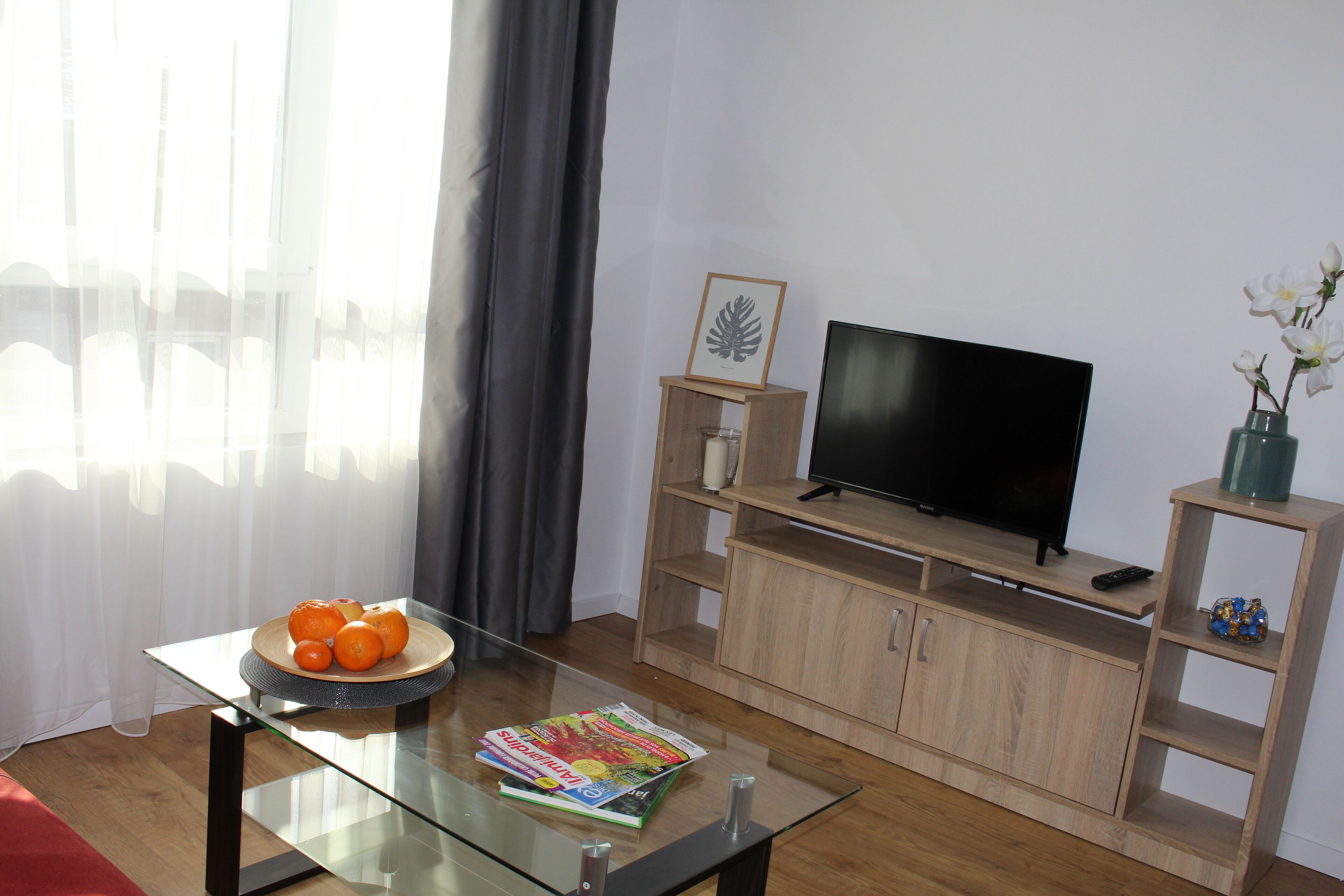 Ein Wohnzimmer mit Glastisch, Flachbildfernseher, Holzunterhaltungseinheit und Blumen in einer Vase.