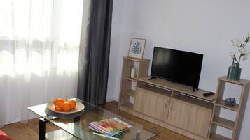 Ein Wohnzimmer mit Glastisch, Flachbildfernseher, Holzunterhaltungseinheit und Blumen in einer Vase.