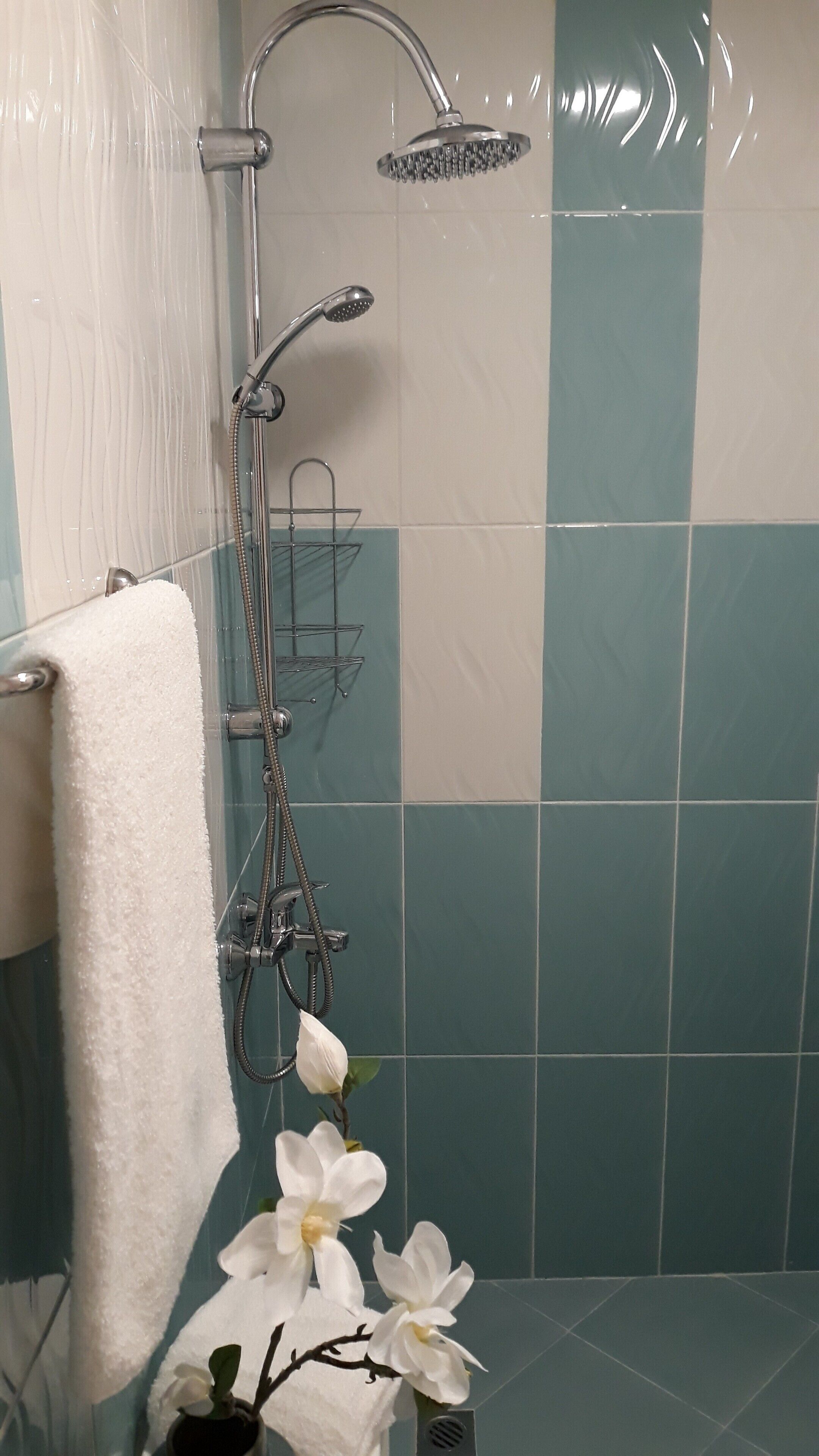A bathroom with a shower, a towel rack, and a small vase with white flowers.