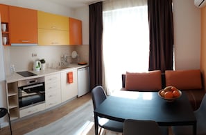 A compact kitchen with modern appliances, a dining area with a table and chairs, and a view of the outdoors through large windows.