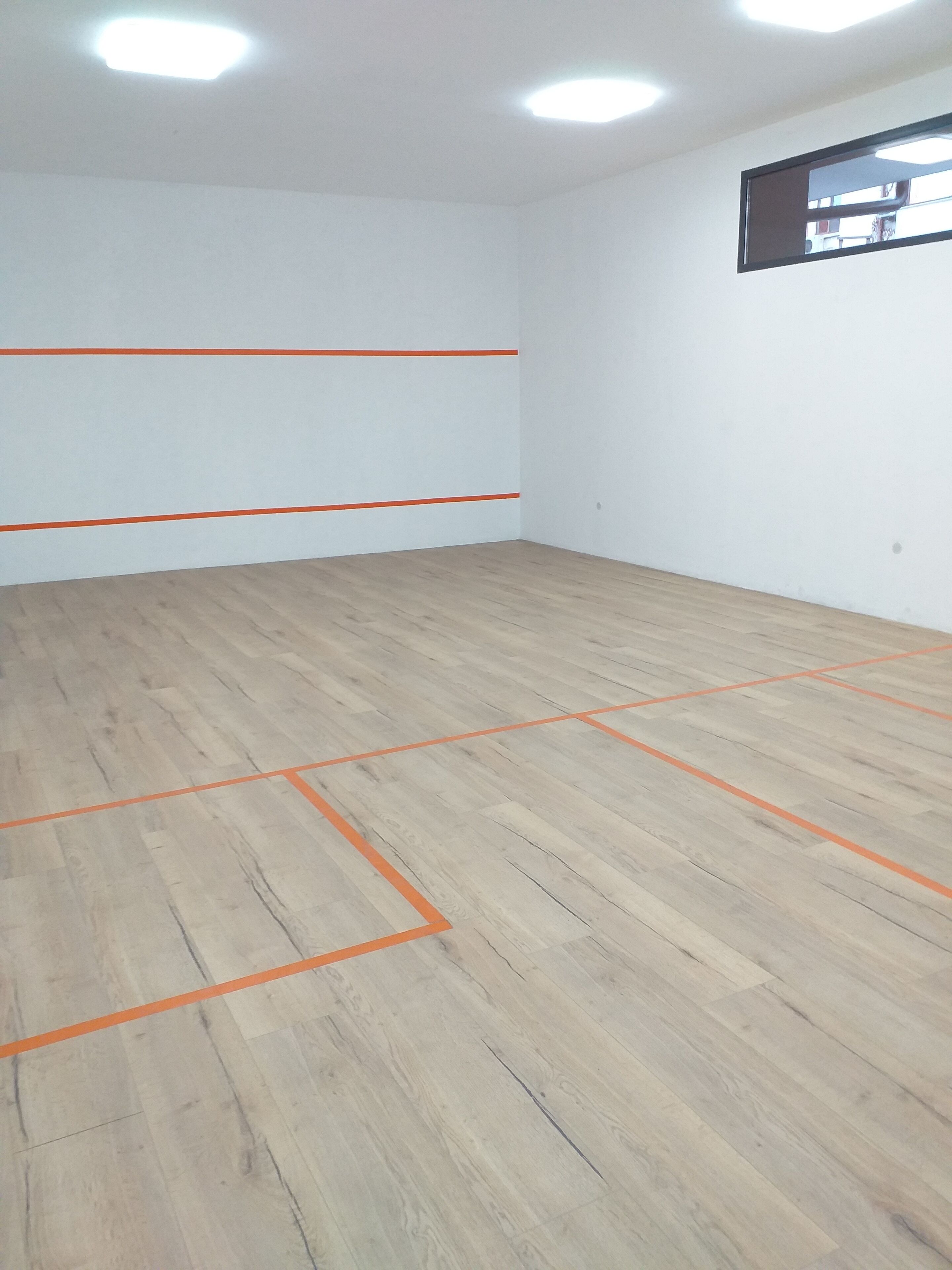 A room with white walls and a wooden floor marked with orange lines, likely for a game or activity.
