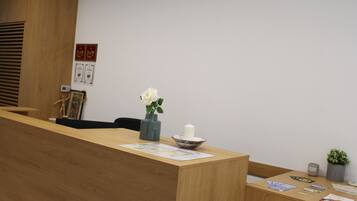 Un mostrador de recepción de madera con un jarrón de flores blancas, una vela y una pequeña planta en maceta. En la pared detrás del mostrador hay diplomas enmarcados.