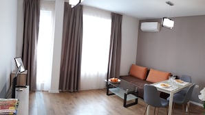 A modern living room with a sofa, a glass coffee table, and a dining table with chairs. There is a piano in the corner, and an air conditioning unit on the wall. - HOTEL39 (Plovdiv)