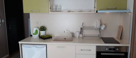Eine kompakte Küche mit Geschirrspüler, Spüle und kleinem Backofen. Über der Spüle befinden sich Schränke und eine Arbeitsplatte mit einem Geschirrgestell.