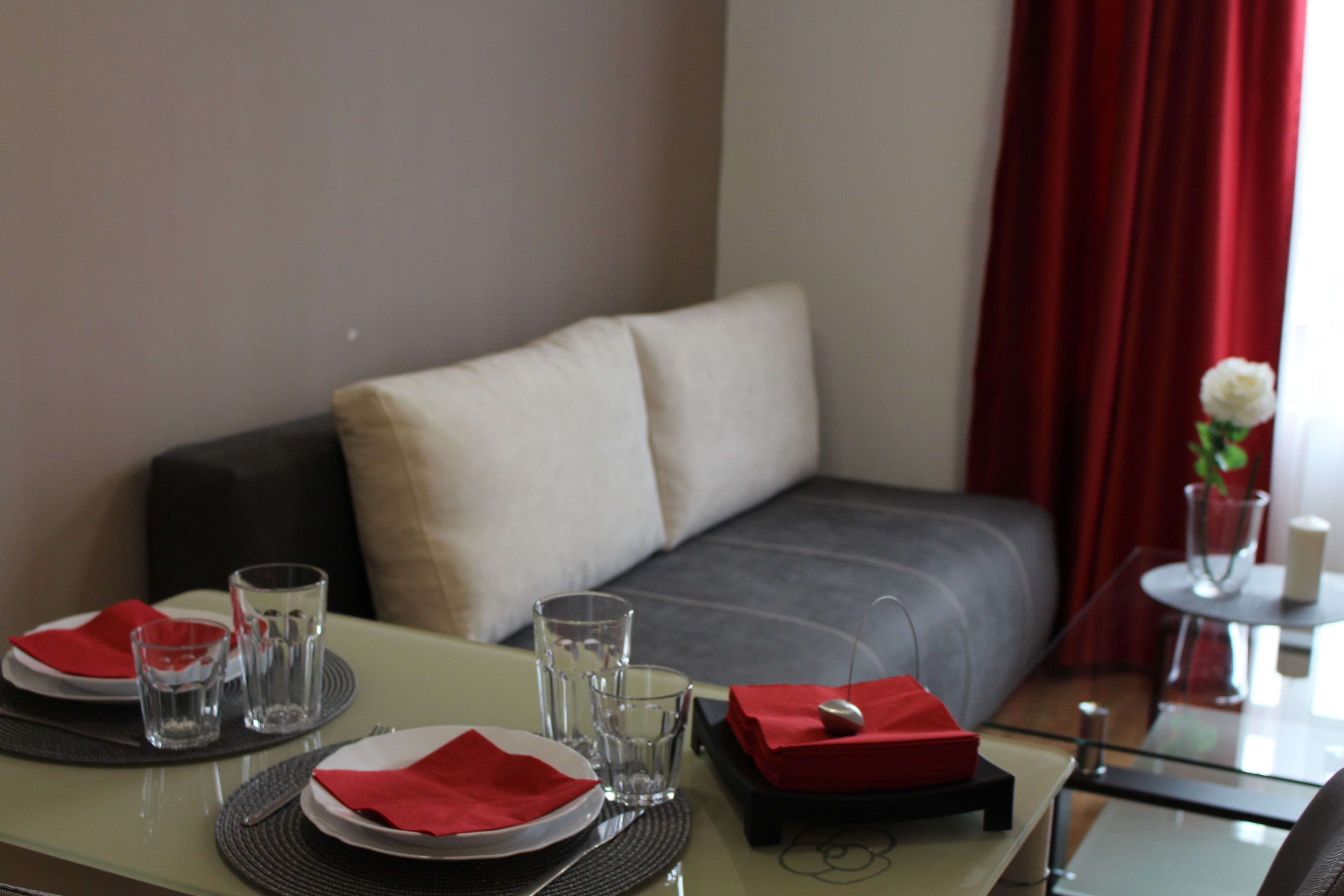 Una mesa de comedor bien puesta con platos, vasos y servilletas, un vaso de agua y un holder rojo para servilletas.
