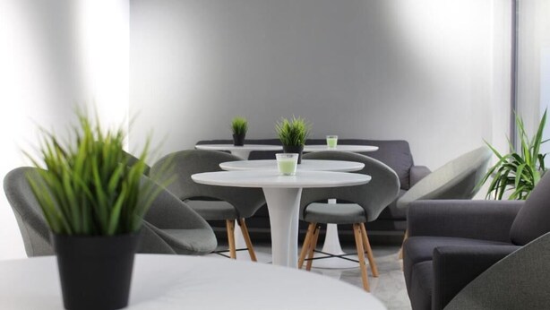 A modern lounge area with round tables, grey upholstered chairs, and small potted plants. - HOTEL39 (Plovdiv)
