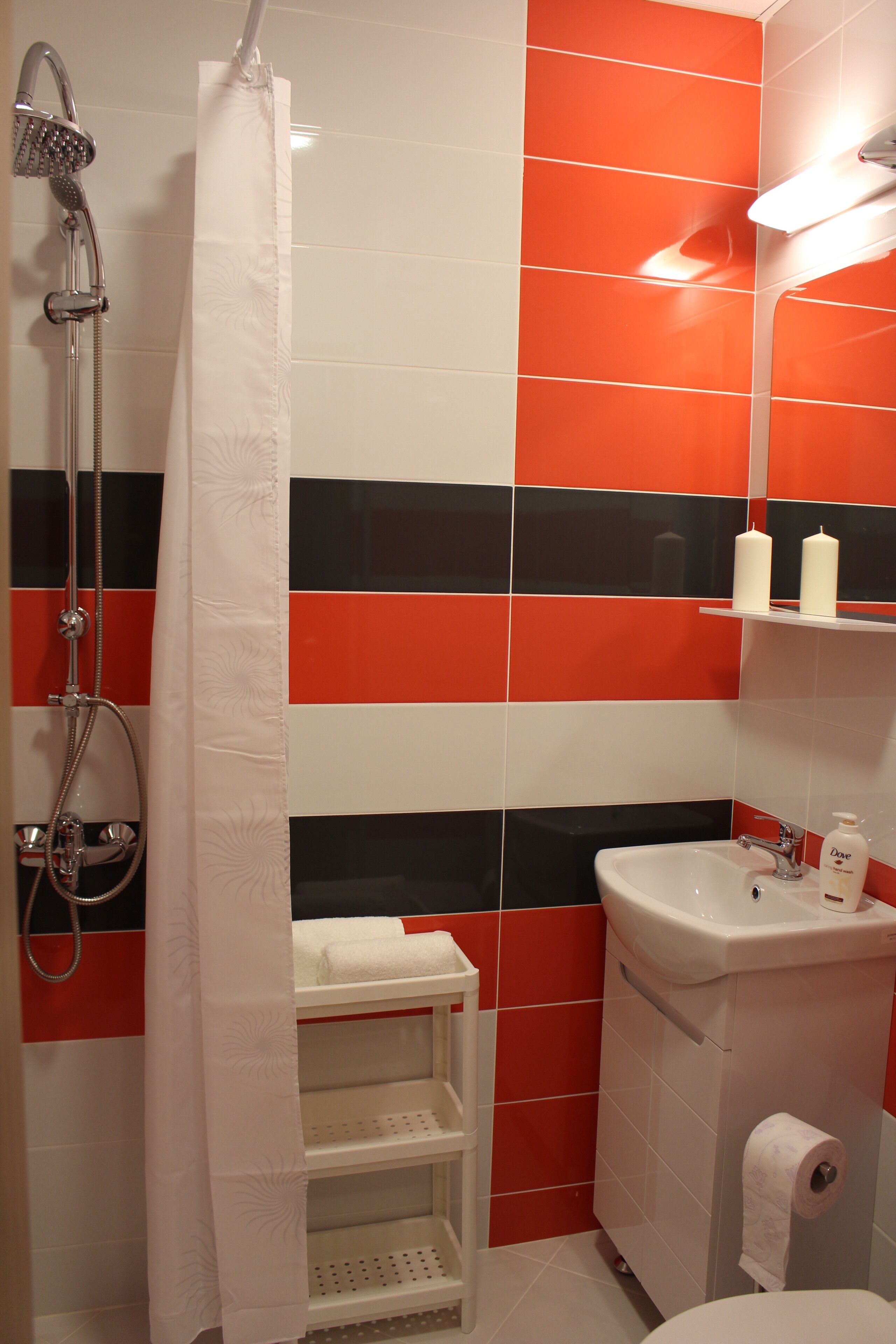 A bathroom with red and black tiles, a shower with a curtain, a sink, and a toilet.