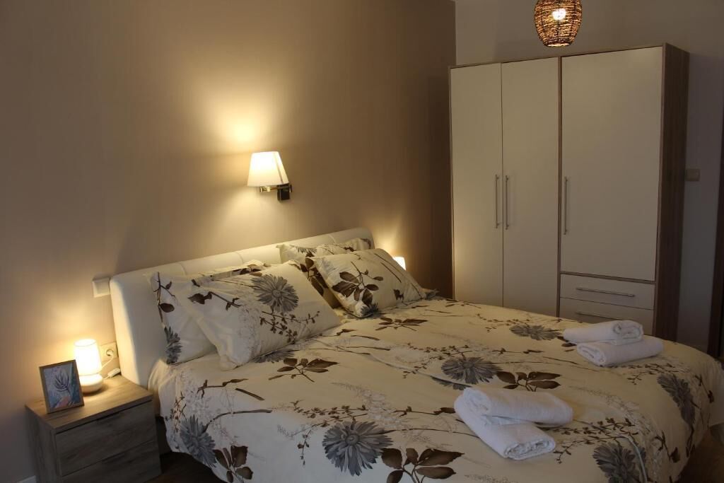 Una cama bien hecha con ropa de cama floral, una lámpara de noche y un armario con espejo.