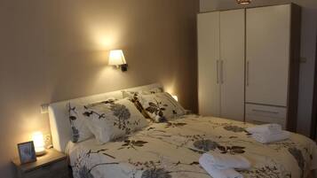 Una cama bien hecha con ropa de cama floral, una lámpara de noche y un armario con espejo.