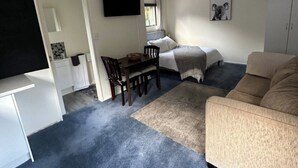 A compact living space with a bed, a sofa, a dining table with chairs, a TV mounted on the wall, and a cabinet. - Country cottage close to airport (pet friendly)  (West Melton)
